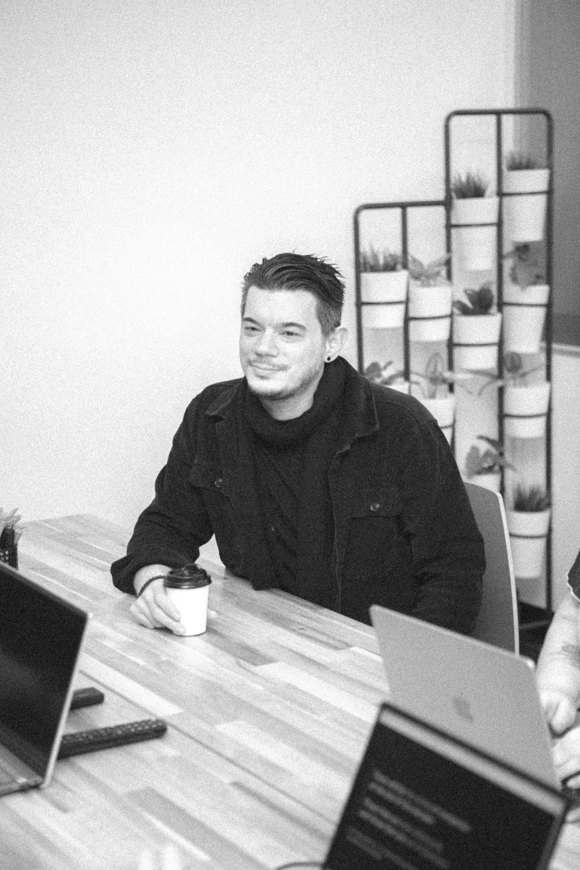 Simon sitting behind a table with a cup of coffee in one hand.